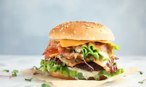 Apetyczny burger z bekonem, serem, pomidorem i sałatą na jasnym tle.