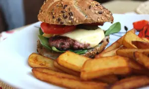 Soczysty burger wołowy z serem, pomidorem i frytkami na talerzu.