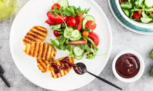 Grillowany ser halloumi z sałatką z pomidorów i ogórka, polany sosem.