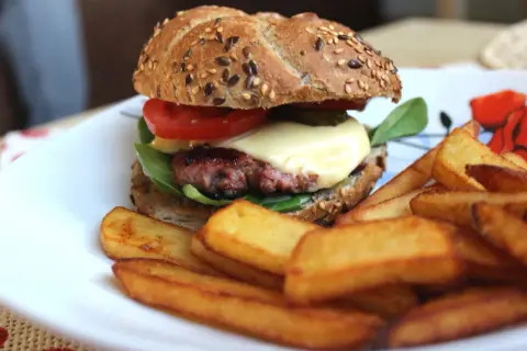 Soczysty burger wołowy z serem, pomidorem i frytkami na talerzu.