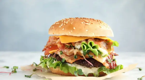 Apetyczny burger z bekonem, serem, pomidorem i sałatą na jasnym tle.