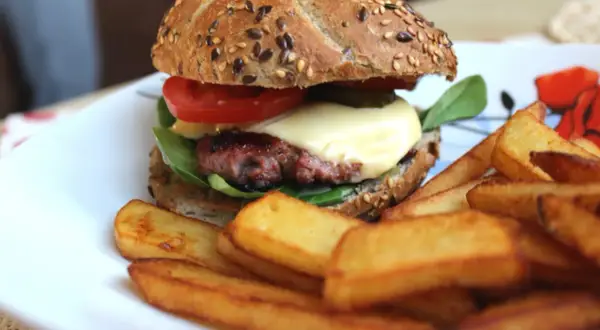 Soczysty burger wołowy z serem, pomidorem i frytkami na talerzu.