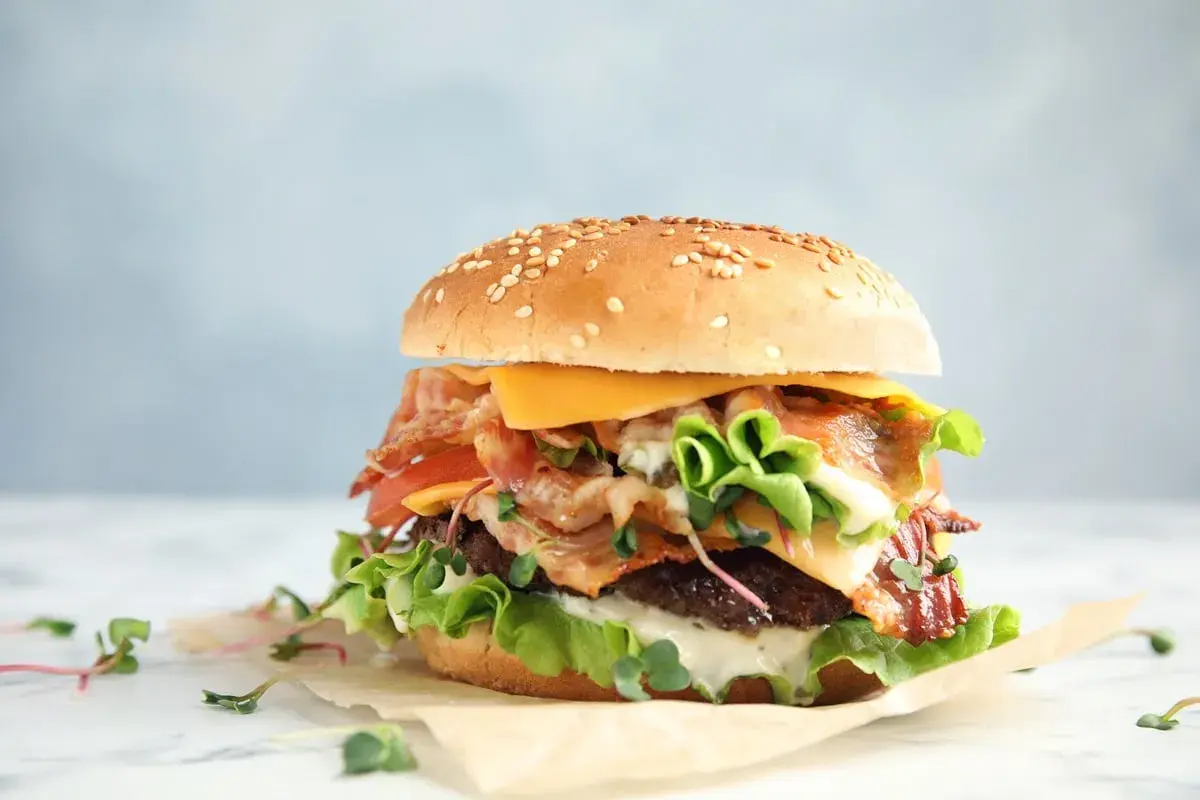 Apetyczny burger z bekonem, serem, pomidorem i sałatą na jasnym tle.
