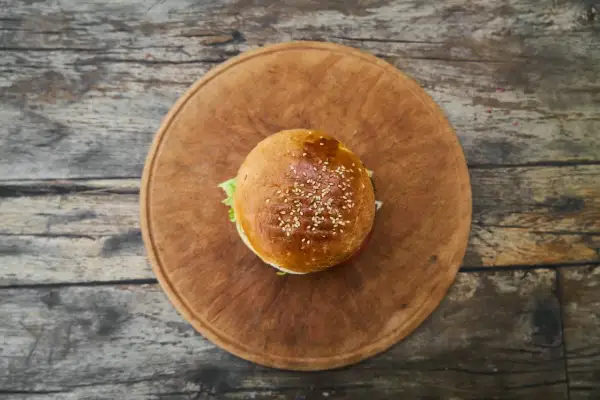 Hamburger z sezamem na drewnianej desce.