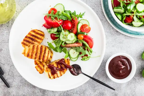 Grillowany ser halloumi z sałatką z pomidorów i ogórka, polany sosem.